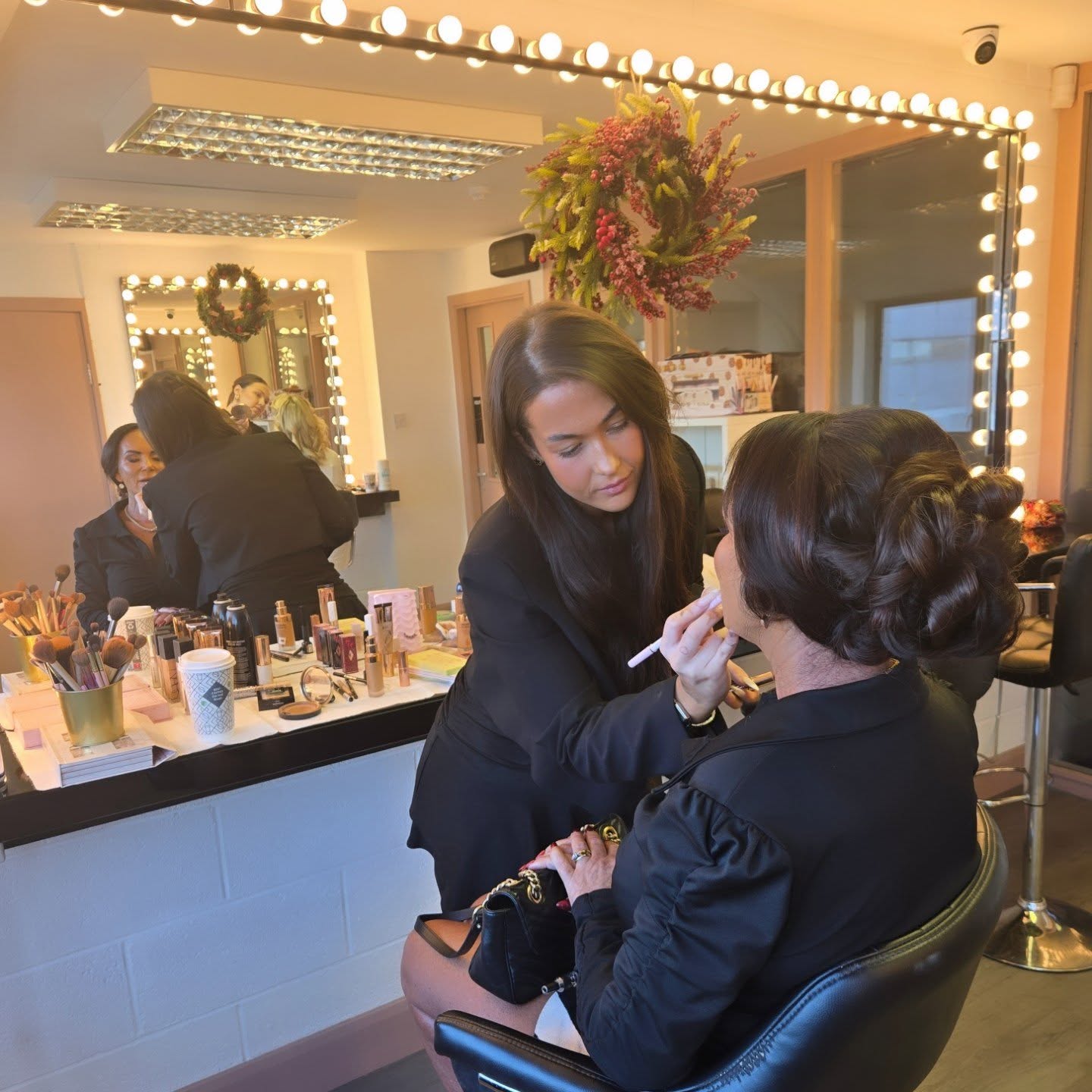 A Luscious stylist applying makeup to a client at the mirrored vanity in the Malahide studio.